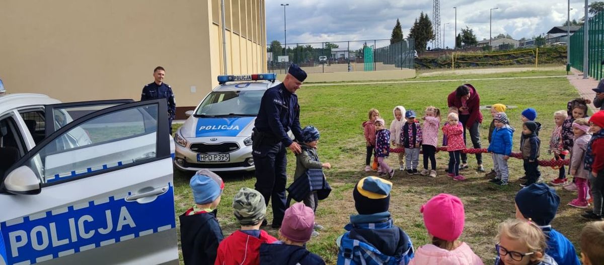 policjant mierzy dziecku kamizelkę wokół stoją dzieci