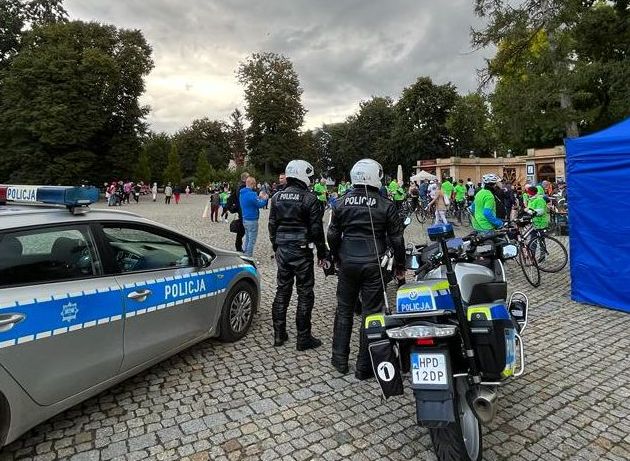 policjanci stojący między radiowozem a motocyklami w tle ludzie na festynie