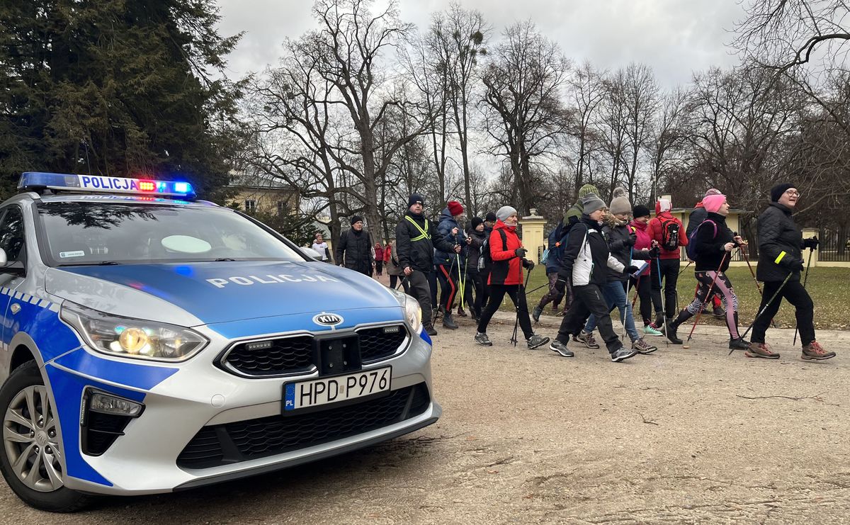 uczestnicy marszu nordic walking przechodzący obok radiowozu