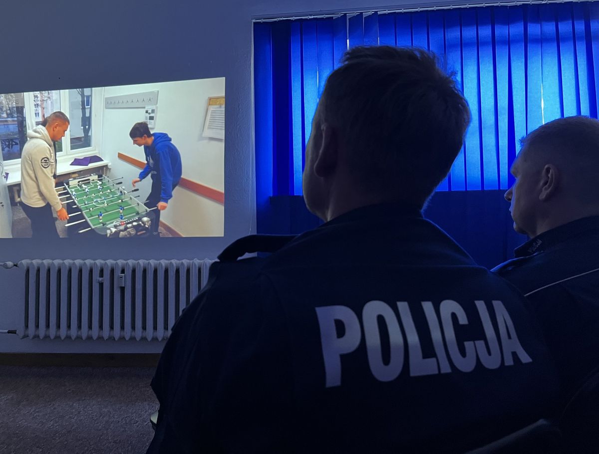 ekran na którym dwóch chłopców gra w piłkarzyki, patrzą na niego policjanci