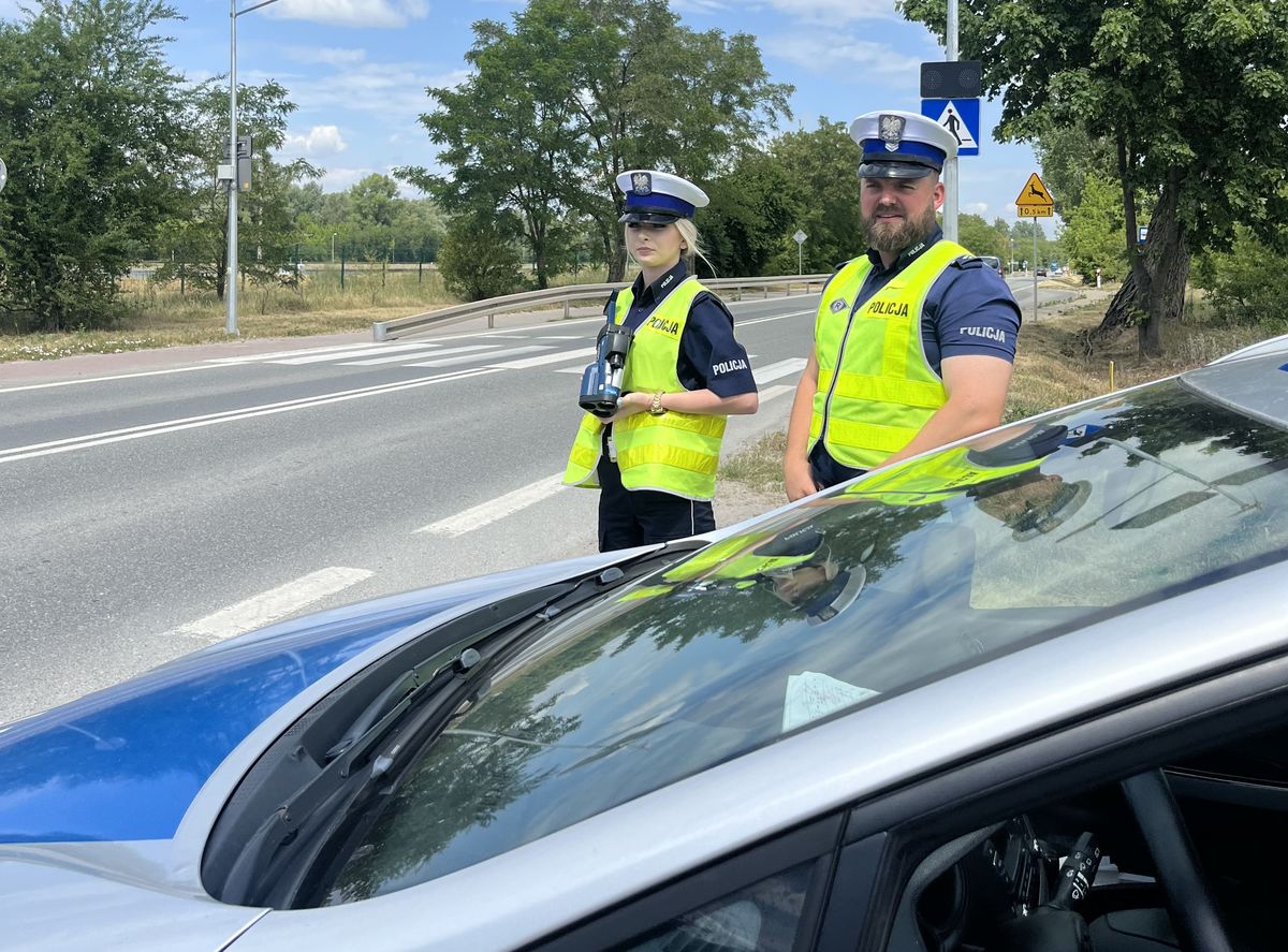 dwoje policjantów obok radiowozu przy drodze