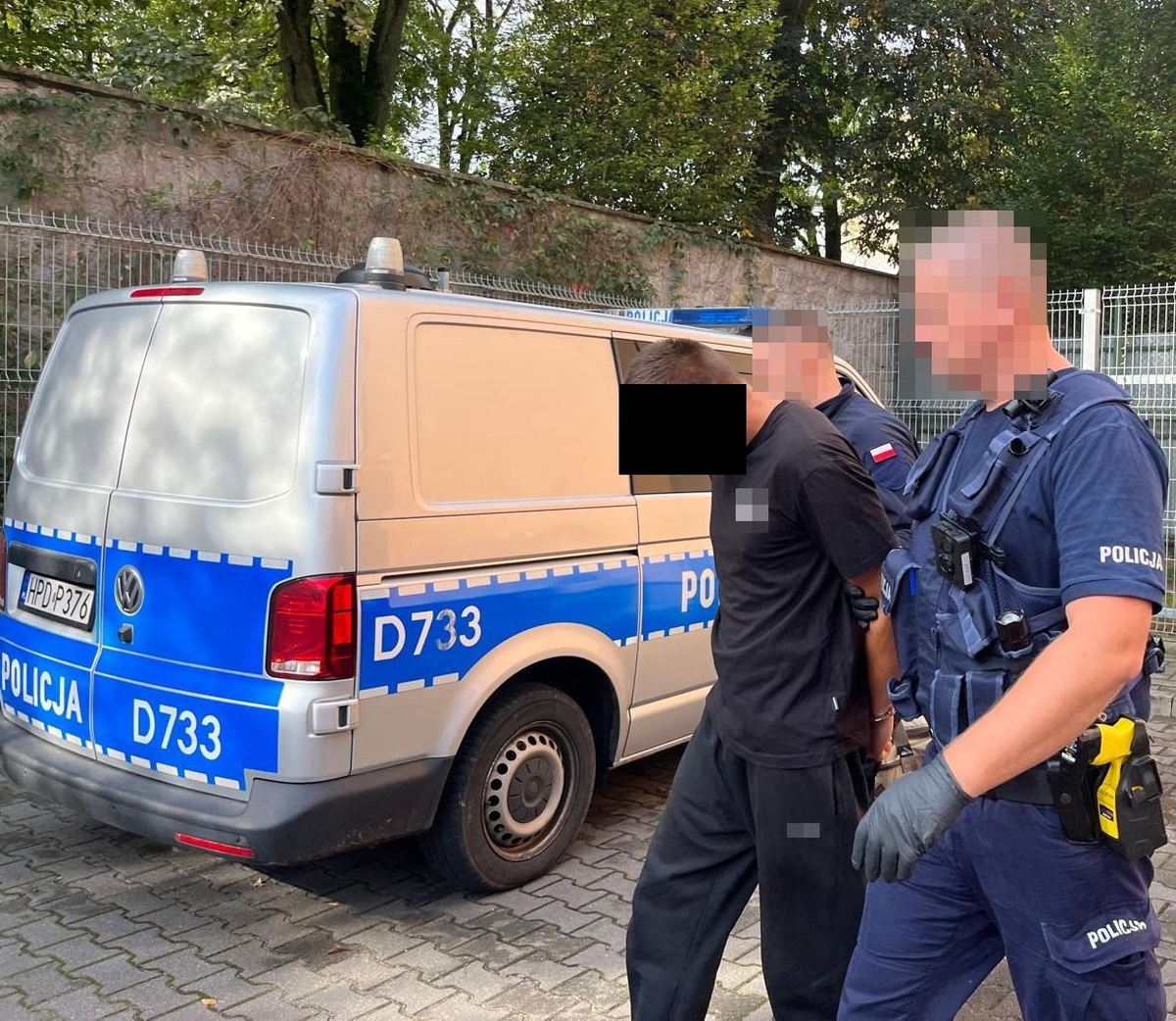 policjanci prowadzący mężczyznę w kajdankach do oznakowanego busa policyjnego