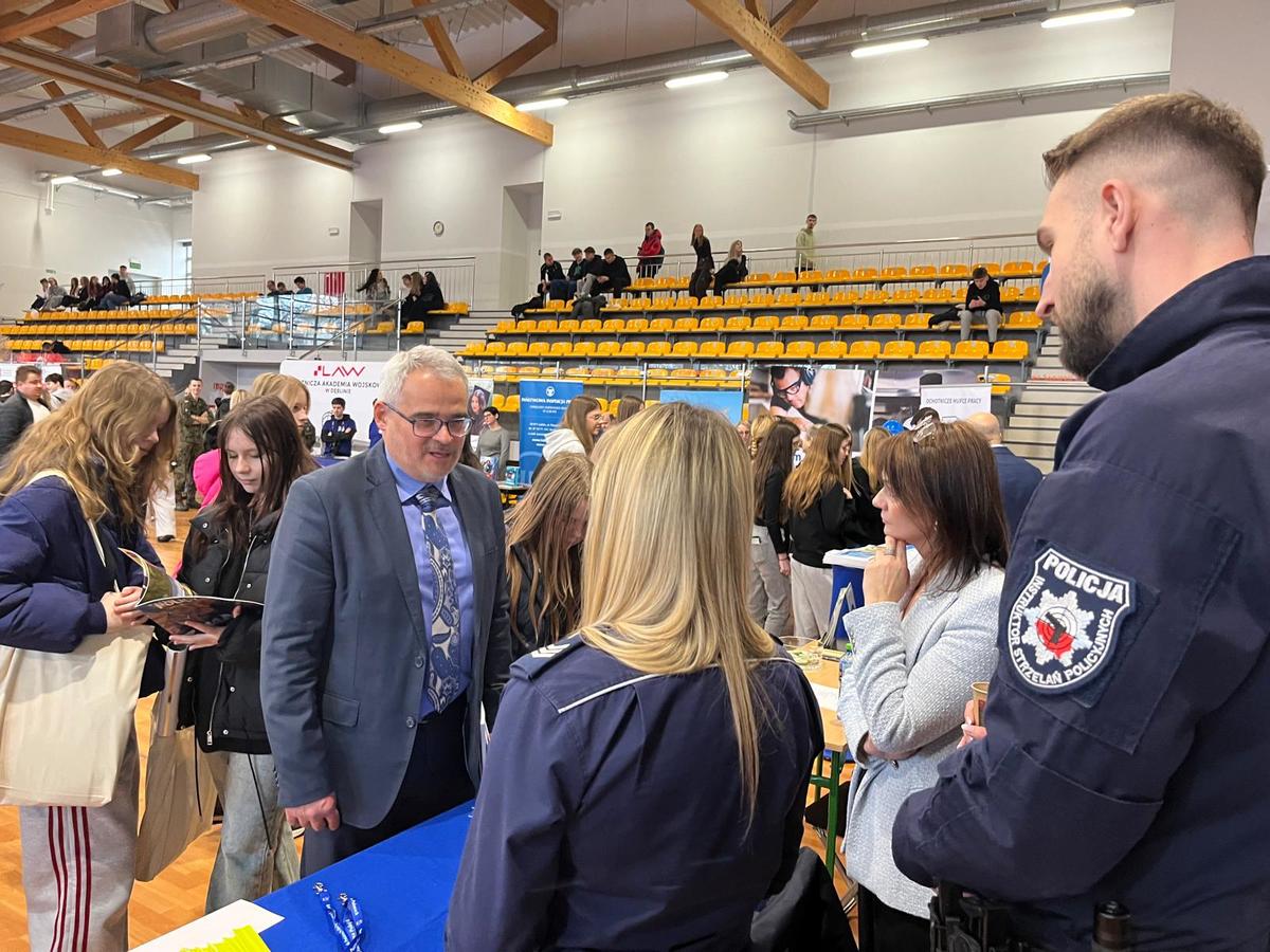Policjant stojący przy stanowisku rozmawiający z ludzmi.