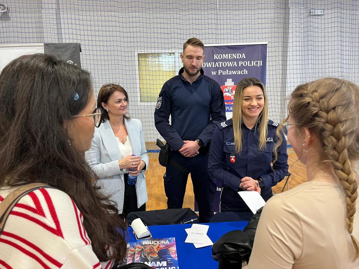 Policjant stojący przy stanowisku rozmawiający z ludzmi.