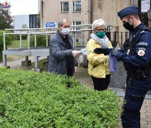 policjant przekazujący maseczki kobiecie i mężczyźnie