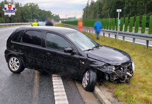 rozbity opel stojący na szosie obok bariery