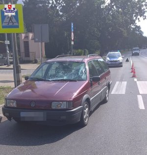 bordowy volkswagen z rozbitą szybą stojący na ulicy, za przejściem dla pieszych, za nim oznakowany radiowóz