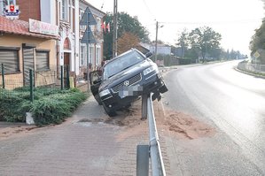 Czarny volkswagen passat zawieszony na barierze przy drodze w tle budynki