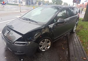 rozbity czarny peugeot na ulicy w tle policjant