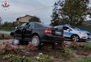 rozbite czarne volvo stojące na rabatce z kwiatami i podjeździe, w tle policyjny oznakowany radiowóz