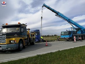 niebieska ciężarówka w rowie obok wyciągający ją dźwig oraz holownik