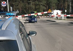 granatowy nissan micra stojący między rogatkami na torach, na pierwszym planie fragment radiowozu