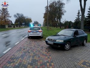 ciemnozielony daewoo stojący na podjeździe za nim radiowóz