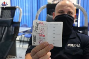 policjant w masce prezentujący legitymację honorowego dawcy krwi