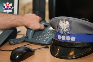 ręka trzymająca słuchawkę od telefonu obok policyjna czapka