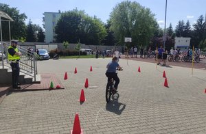 dziecko na rowerze jadące między pachołkami na placu przyglądający mu się policjant i inne dzieci