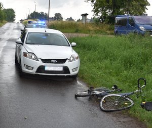 biały ford na szosie przed nim pokrzywiony rower w tle światła radiowozu