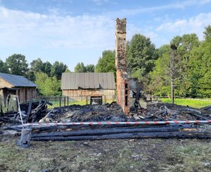 zwęglone resztki spalonego domu w tle zabudowania gospodarcze