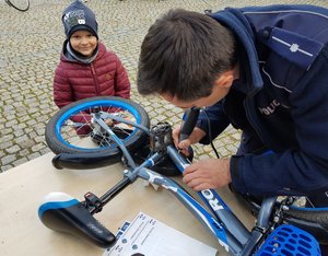 policjant znakujący rower obok niego stoi mały chłopiec