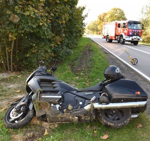 czarny motocykl na poboczu w tle samochód ciężarowy straży pożarnej