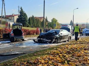 rozbity czarny mercedes na ulicy obok skoda z otwartym bagażnikiem w tle karetka i policjant