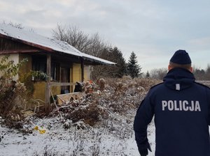 policjant i zniszczony drewniany dom