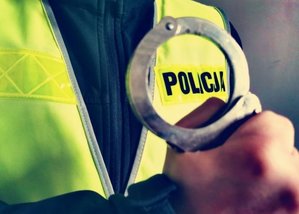 ręka trzymająca kajdanki na wysokości napisu policja na kamizelce odblaskowej