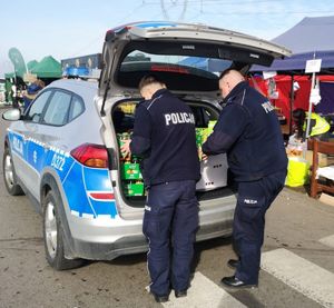 dwóch policjantów przy radiowozie rozładowuje pudła ze słodyczami