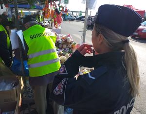 policjantka stojąca obok stoiska z pomocą dla uchodźców przed nią dwoje wolontariuszy wypakowuje maskotki