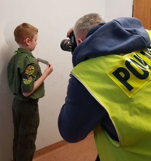 mężczyzna w kamizelce z napisem policja wykonuje zdjęcie chłopcu w mundurze zucha