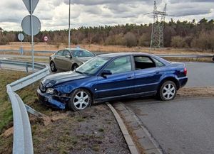 granatowe rozbite audi stojące przed barierą w tle cywilny beżowy radiowóz z lampą na dachu