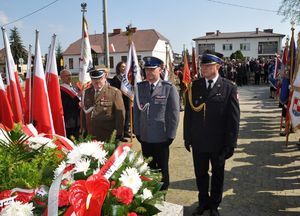 komendanci policji straży i wojska stojący przed pomnikiem z wiązankami