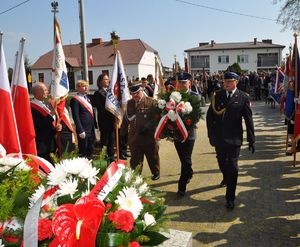 komendanci idący w stronę pomnika z wiązanką biało czerwonych kwiatów