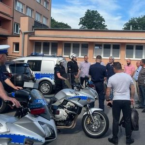 grupa osób przed budynkiem obok dwa policyjne motocykle i radiowóz