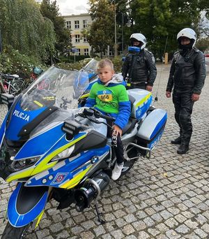 chłopiec siedzący na policyjnym motocyklu obok stoi dwóch policjantów