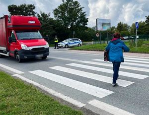 kobieta przechodząca po przejściu, w tle radiowóz przed przejściem stoi samochód dostawczy