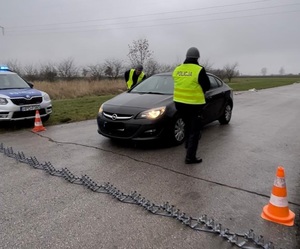 dwóch policjantów zatrzymuje samochód na drodze, na której leży rozciągnięta kolczatka