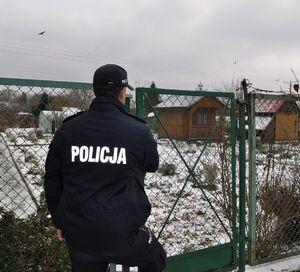 policjant przed bramą ogródków działkowych