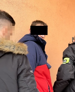 policjanci prowadzący zatrzymanego mężczyznę z zasłoniętymi oczami