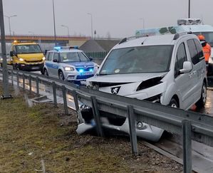 rozbity szary peugeot koło barierki w tle radiowóz i pomoc drogowa zajawka