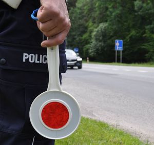 tarcza do zatrzymywania pojazdów w ręce policjanta w tle droga