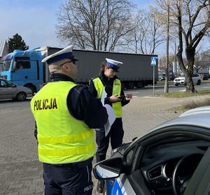 policjanci obok radiowozu przy drodze w tle jadą samochody