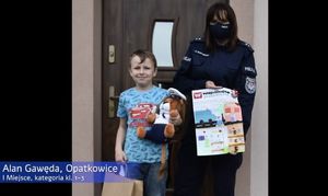 policjantka prezentująca plakat obok chłopiec z maskotką