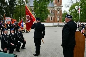 strażak ze sztandarem przed nim trzech klęczących strażaków