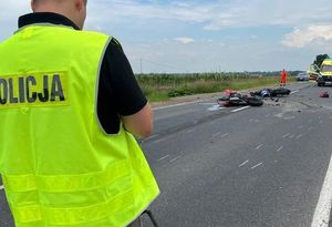 policjant w żółtej kamizelce piszący protokół, w tle dwa rozbite motocykle na jezdni