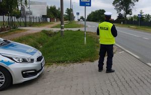 radiowóz przy drodze obok niego policjant patrzący w kierunku nadjeżdżającego samochodu