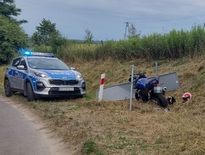 niebieski motocykl stojący obok uszkodzonego znaku drogowego obok radiowóz