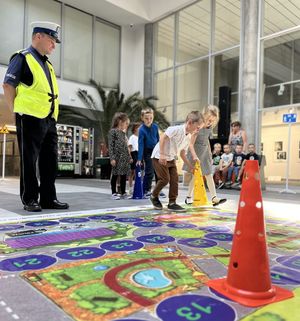 policjant patrzący na dzieci idące z pachołkiem po planszy
