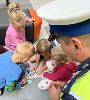 dzieci układają znak drogowy z puzzli, policjant się przygląda