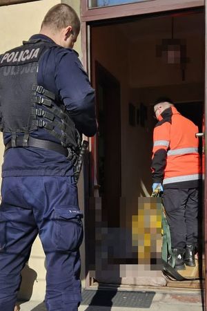 policjant stojący przed wejściem do domu w tle ratownik medyczny